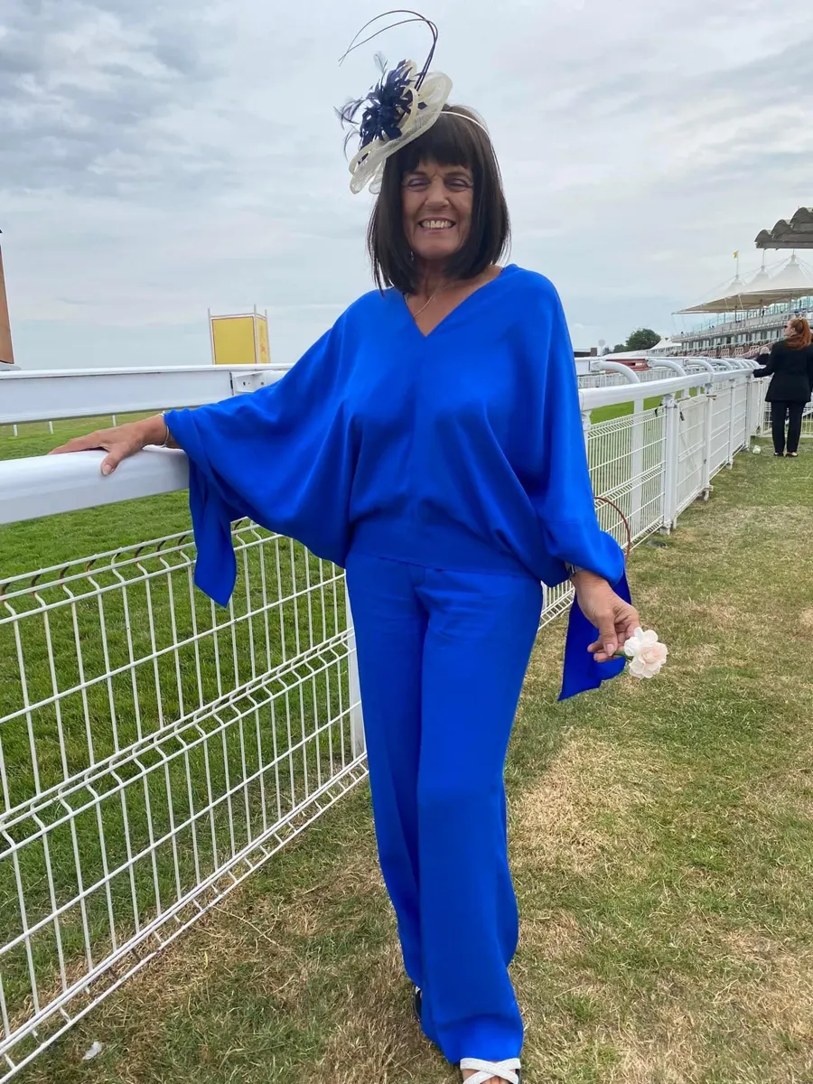 Linda in a blue outfit beside the rail at a racecourse
