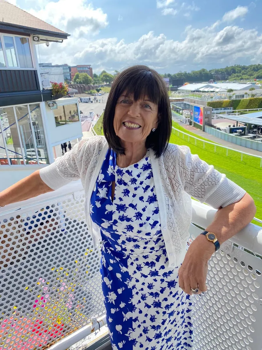 Linda smiling on a racecourse balcony