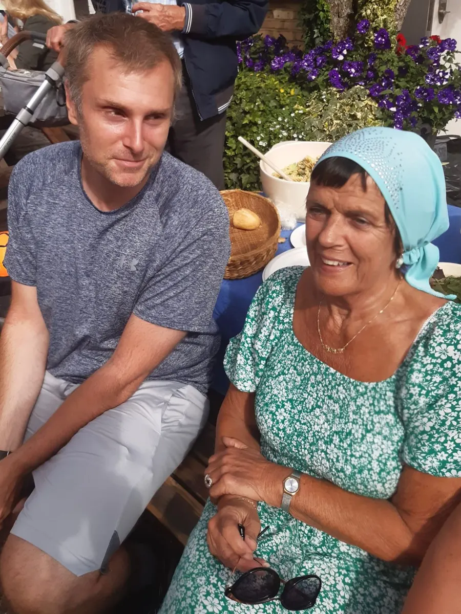 Linda wearing a headscarf, sitting with a young man outdoors